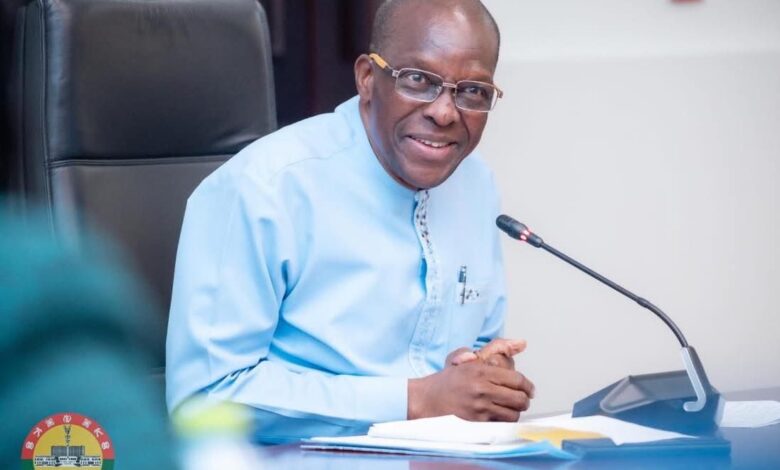 Speaker of parliament speaking into a microphone while seated at a meeting table, smiling during a formal discussion.