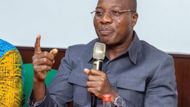 Mahama Ayarega Seated and speaking into a micophone.